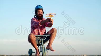 长胡子的滑稽男人在天空背景下骑着儿童自行车玩得很开心。 一个长胡子的滑稽男人骑着儿童自行车
